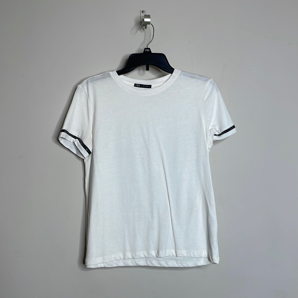 White tee with beaded details on the sleeves.